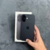 Rear view of a Black iPhone 17 non pta held against its official retail box, showing the dual rear camera module, matte back glass, and retail packaging.